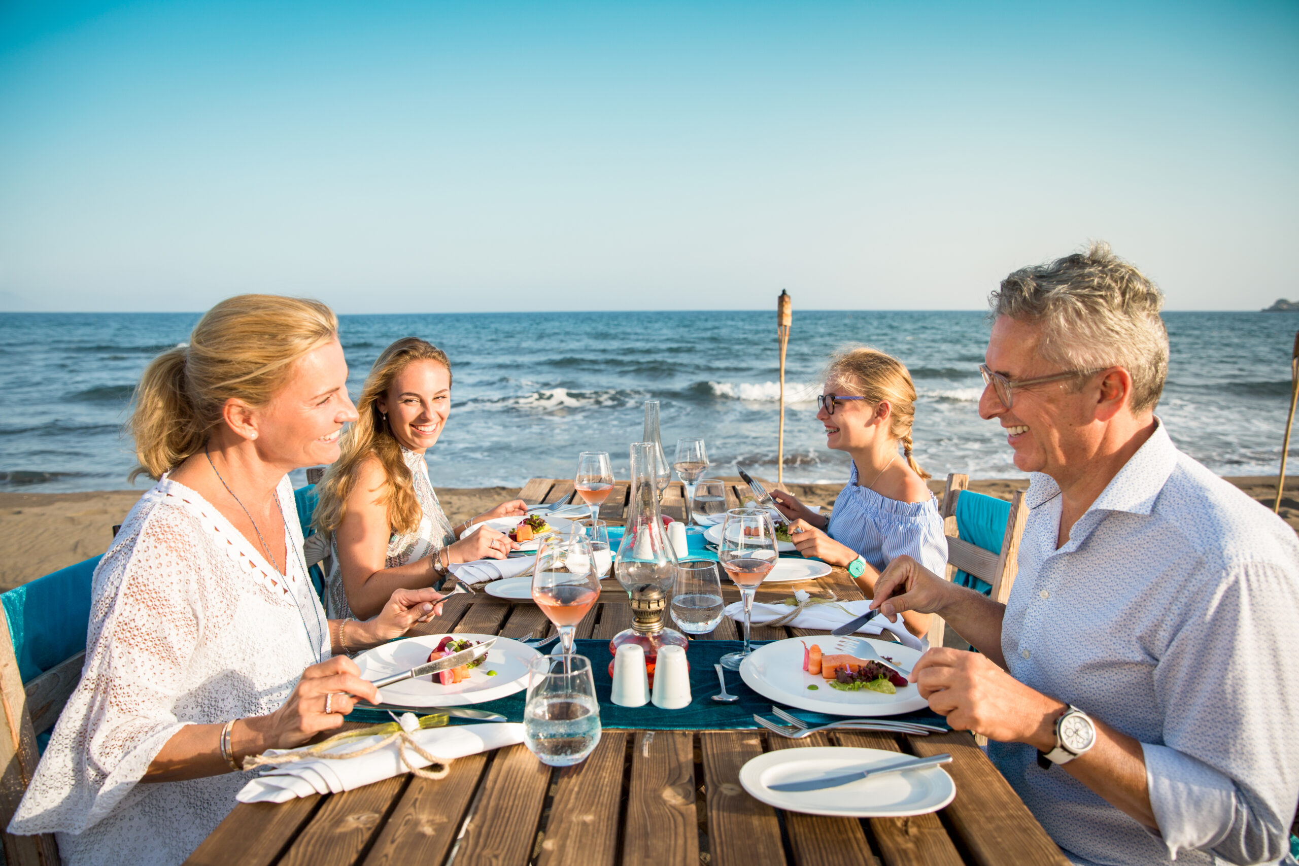 Familie sitzt zum Essen an einem Tisch direkt am Strand.