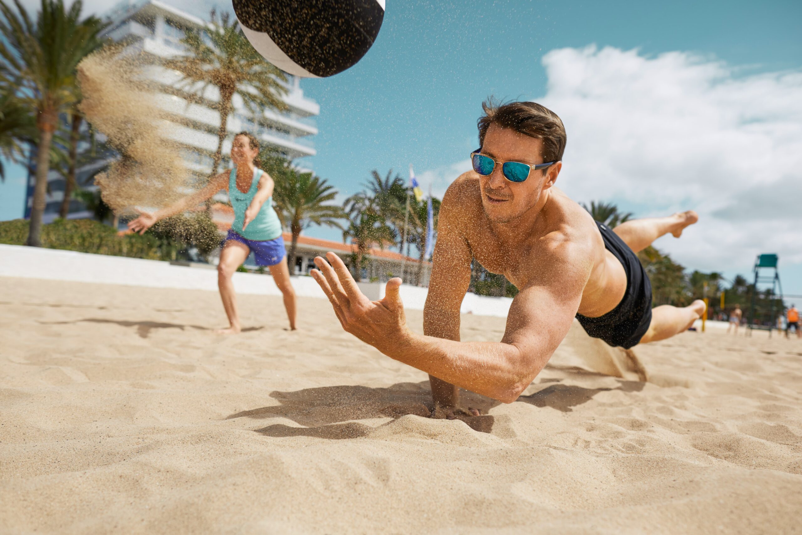 Ein Mann spielt Volleyball und lässt sich dabei in den Sand fallen.
