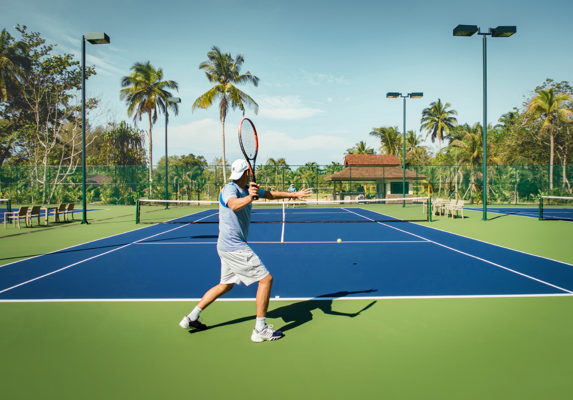 Tennisspieler auf Platz mit Palmen im Hintergrund